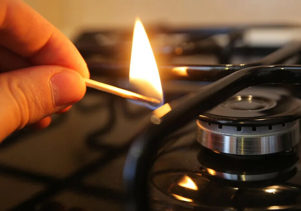 Человек подносит спичку к газовой конфорке. 